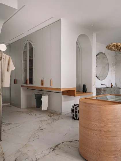 A wider view of the walk-in area, showing the custom island dresser, open hanging racks, and the seamless flow into the marble-clad bathroom.
