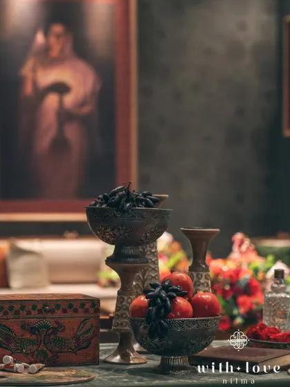 A tabletop arrangement featuring bowls of dark grapes and pomegranates, echoing the rich colors and still-life elements of Raja Ravi Varma's paintings.