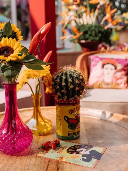 A close-up of a table centerpiece, featuring sunflowers, red chilies, and a cactus in a quirky repurposed can. These details are key to the authentic Mexican fiesta theme.