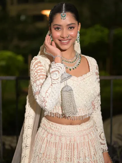 A happy and radiant bride in her beautiful white and pink lehenga. The makeup is fresh and glowing, and the emerald jewelry adds a pop of color.