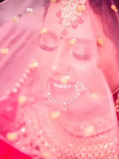 A dreamy and joyful bridal portrait. The bride is smiling with her eyes closed, seen through her pink veil, which creates a soft, romantic, and colourful effect.