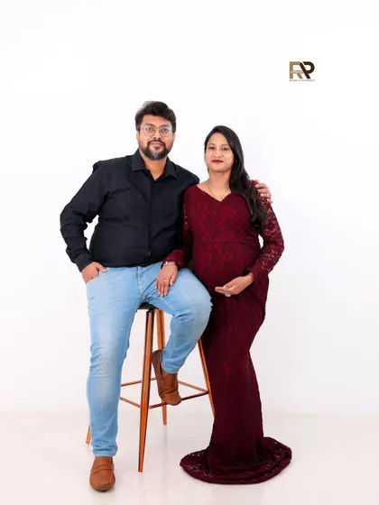 A classic and confident couple's portrait. The mom-to-be glows in a deep red lace gown, a modern yet elegant choice, while her partner stands proudly by her side.