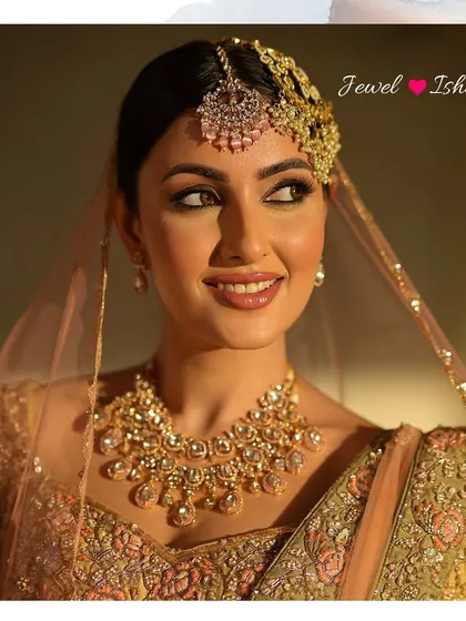 A beautiful, soft-focus portrait of the bride looking away from the camera. The lighting highlights the sparkle of her polki necklace and the delicate embroidery on her outfit.