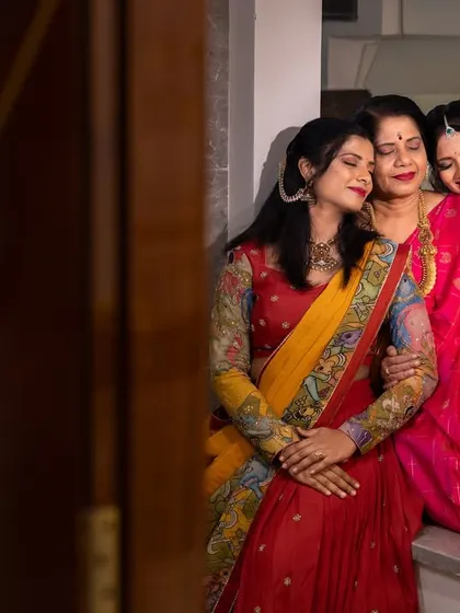 A beautiful, candid moment of three women sharing a warm embrace on the stairs of a new home, their colorful sarees adding to the festive atmosphere.