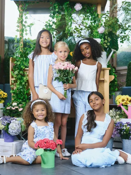 A group portrait for a spring/summer collection. The set is filled with flowers, creating a fresh and vibrant atmosphere that complements the clothing.