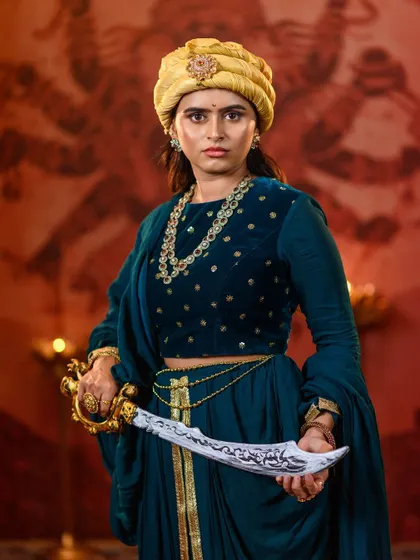 A direct, confrontational pose that showcases the ornate details of the sword and the rich texture of the teal velvet top. We provide high-quality props to complete your character transformation.