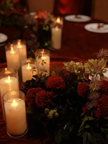 A close up of a table centerpiece from the "Red Hue" engagement. We combined deep red flowers with textured greenery and pillar candles in glass hurricanes for a romantic, moody effect.
