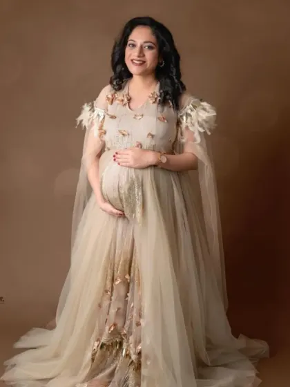 It's all in the details. This exquisite beige gown features delicate 3D floral and feather embellishments and a sheer, flowing cape, offering a soft, romantic, and uniquely detailed look for your special occasion.
