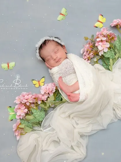 A beautiful overhead shot of a baby swaddled in white, lying on a bed of pink flowers and surrounded by fluttering butterflies. A truly magical composition.