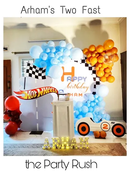 Arham is 'Two Fast' with this cool and modern Hot Wheels party. The setup features a road-themed backdrop, a race car cutout, and a dynamic orange and blue balloon arrangement.