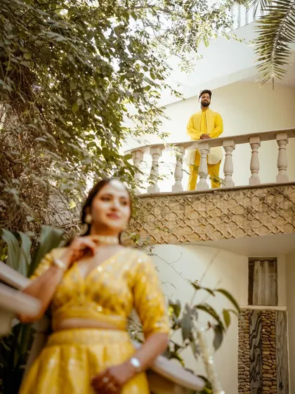An artistic shot of the couple, with the bride in the foreground and the groom on a balcony above, creating a sense of story and anticipation.