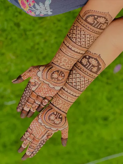 A beautiful outdoor shot showcasing a full bridal design with personalized elements. The natural light brings out the fresh henna paste's texture and detail.