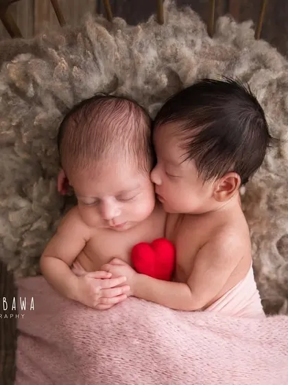 A tiny kiss between twins. This incredibly sweet moment shows one newborn twin snuggling close and appearing to kiss her sister's cheek. These are the magical moments I live to capture.