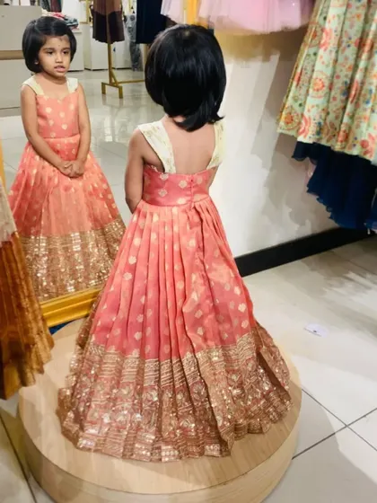 That mirror-check moment. She's admiring her custom peach and gold brocade frock, and honestly, I can't blame her. The pleated skirt and detailed border are designed for maximum impact.