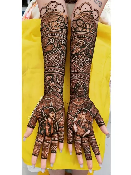 The bride and groom are depicted in individual portraits on each palm, framed within ornate arches. The design is complemented by peacock and lotus patterns.