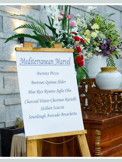 A menu board for our "Mediterranean Marvel" offerings, elegantly displayed on a wooden easel and flanked by floral arrangements, signaling a gourmet experience to come.