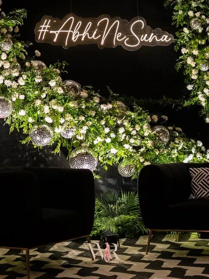 The couple's custom hashtag, #AbhiNeSuna, in a stylish neon sign against a backdrop of white florals and disco balls. It's a modern, fun, and personalized element for their photo booth.