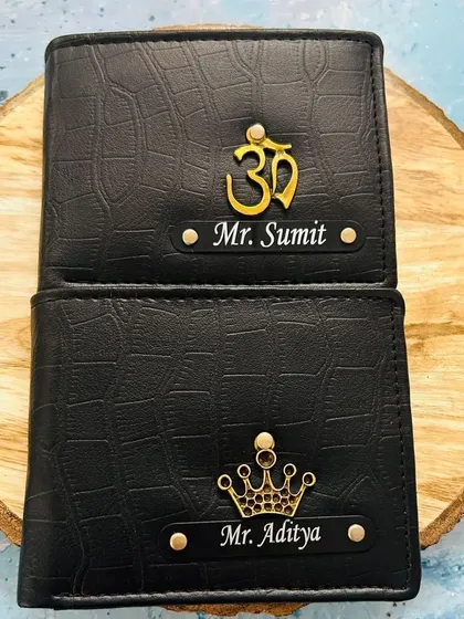 Two black croc-textured wallets with different spiritual and classic charms, one with an "Om" symbol and the other with a crown.