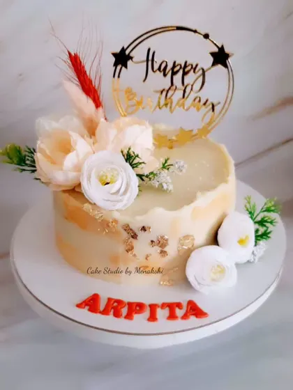 A pretty no-fondant cake in shades of peach and gold. This design is decorated with delicate flowers and a custom topper, making it a warm and elegant choice for a birthday.