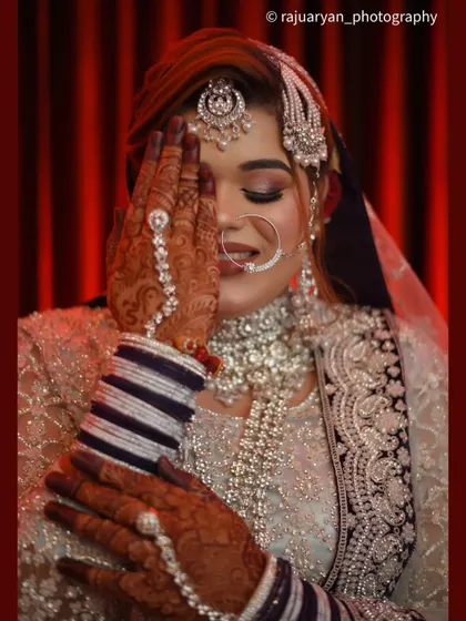 A close-up portrait focusing on the bride's shy smile and beautiful henna-adorned hand. This 'haya' or modest pose is a classic in bridal photography, full of grace and emotion.