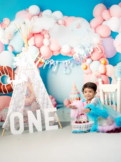 A moment of sweet curiosity during her first birthday celebration. This little one is ready to dig into her cake, surrounded by a dreamy setup of balloons and a lace teepee.