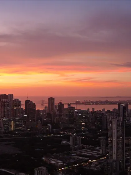 The Bandra-Worli Sea Link is visible in the distance as the sun sets over Mumbai, painting the sky in vibrant shades of orange and pink.