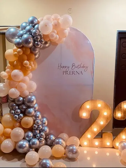 A stylish 22nd birthday decoration for Prerna. This home setup features an arched backdrop, a balloon garland in peach and silver, and large light-up marquee numbers.