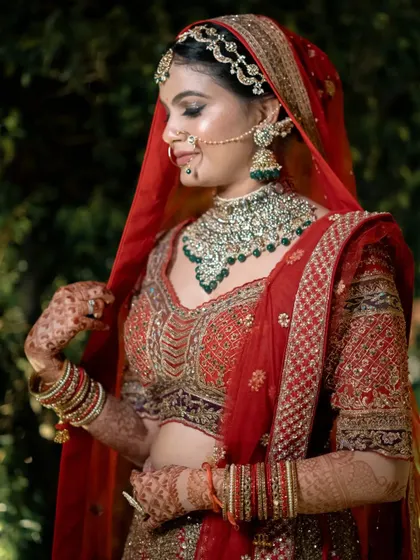 A beautiful outdoor bridal portrait, with the bride adjusting her veil against a lush green background.