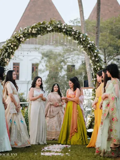 A candid moment during the bridal entry, capturing the interactions between the bride and her bridesmaids under a floral arch.