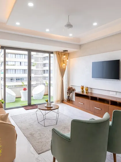This living room opens up to a beautiful balcony with a green turf, blurring the lines between indoor and outdoor living. The neutral furniture and wooden TV console maintain a warm and natural feel.