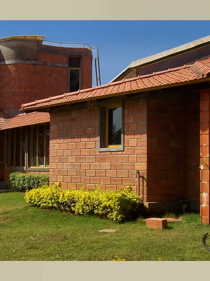This view of a farmhouse shows how different building volumes connect around a central green space. The use of hollow clay blocks and Mangalore tiles creates a cohesive architectural language that is both sustainable and visually warm.