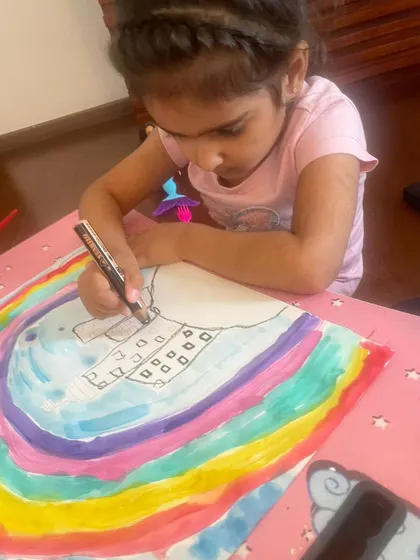 A young artist carefully adds details to her rainbow-themed drawing during an online session.