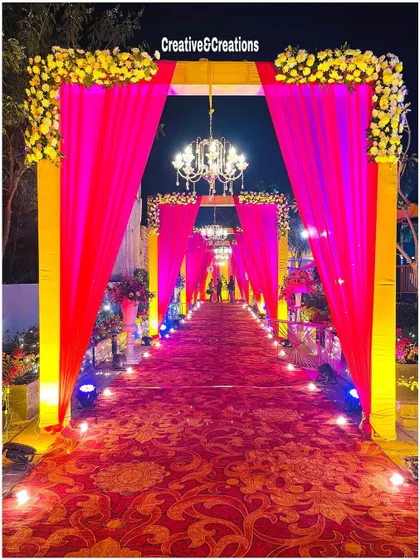 A bold and beautiful entrance with bright pink drapes and a golden frame. The pathway is lit with blue and yellow lights, creating a colorful and high-energy start to the event.