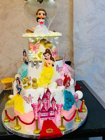 A truly magical multi-tier Disney Princess cake for a grand 5th birthday celebration. This design features a castle, a red carpet entrance, and beloved princesses like Belle, Ariel, and Cinderella, all brought together in one spectacular, edible creation.