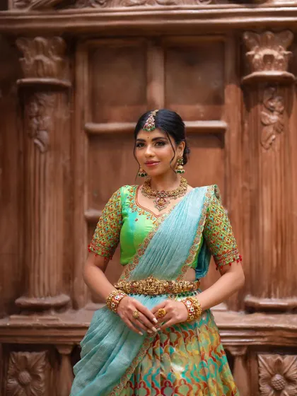 A beautiful portrait featuring a light blue and green half saree. The traditional wooden door in the background adds a rustic and elegant touch.
