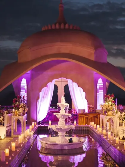 A 'Sufi Night on a Palace Rooftop' was inspired by the groom's white sherwani. The decor featured a stunning white fountain, candlelit water bodies, and purple uplighting against the palace dome, creating a mystical and romantic ambiance.
