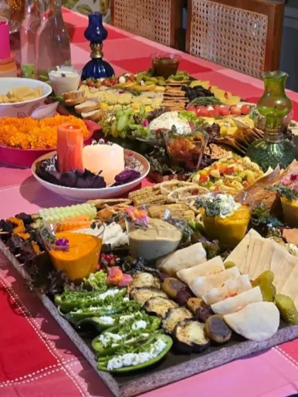 Our party spread runs across a pink tablecloth, with crackers, fruit, dips and savoury bites arranged around candles and flowers.