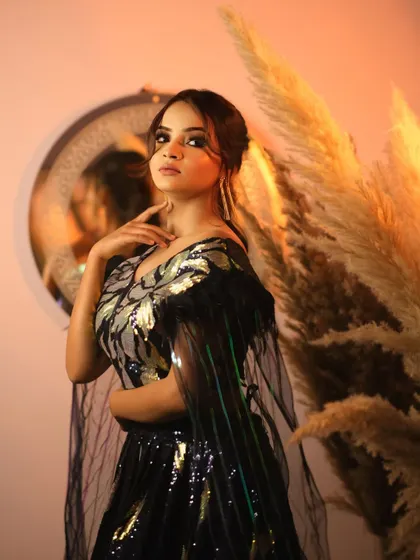 A confident and poised portrait. The model looks directly at the camera, showcasing her stunning makeup and the intricate design of her glamorous outfit.