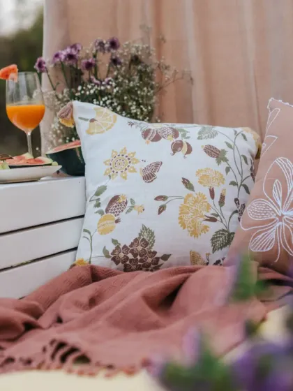 A close-up of our floral cushion cover, paired with a soft pink throw. This combination is perfect for adding a touch of warmth and elegance to any corner of your home.