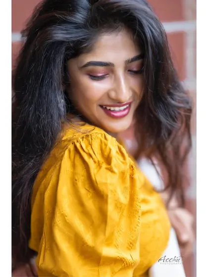 A close-up shot that captures a genuine, happy smile. The soft, natural light and the bright yellow top create a warm and cheerful vibe.