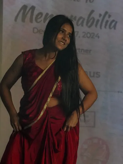 A student performs an expressive dance in a simple yet elegant red saree.