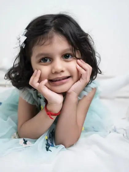 A sweet girl lying on a bed, resting her chin in her hands. Her direct gaze and gentle smile create a simple yet captivating portrait.
