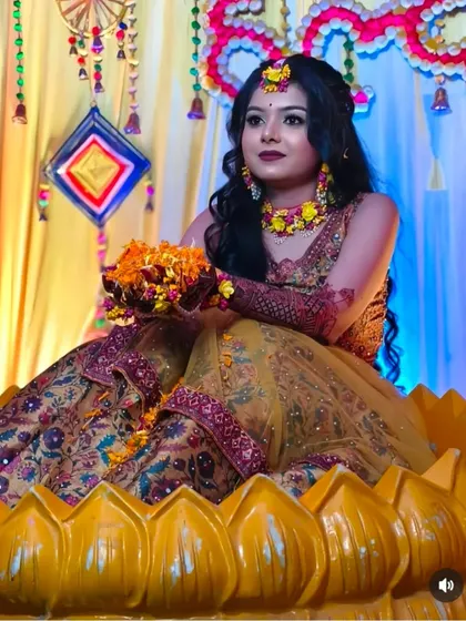 A creative shot of a bride at her Haldi or Mehndi ceremony, sitting in a giant lotus prop, her henna-adorned hands holding flowers.