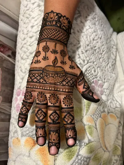 A perfect Diwali mehendi, with a brightly shining diya at its center. The design is complemented by auspicious swastika symbols and lotus patterns on the fingers.