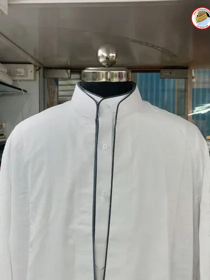 A white saya kurta with dark grey piping. This detail along the collar and placket gives the traditional garment a modern and charismatic look.