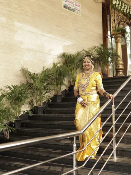 The bride posing on a staircase, the yellow of her saree and the gold of her blouse creating a bright and auspicious look.