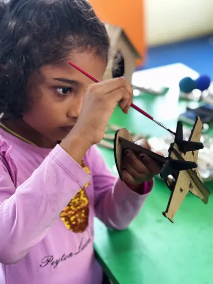 A close-up of a young girl's intense focus as she paints her model. These moments of deep engagement are what our workshops are all about.