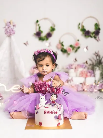 A magical first birthday cake smash. This little girl is exploring her beautiful butterfly cake in an enchanted purple garden.
