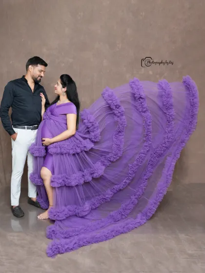 A glamorous studio shot of a couple with a flowing purple ruffled gown. The dramatic lighting and pose create a high-fashion feel.
