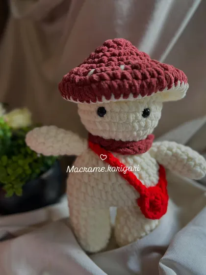 Meet our little mushroom friend. This amigurumi toy features a big mushroom cap, a tiny red scarf, and a matching bag. It’s a whimsical character straight out of a fairytale.